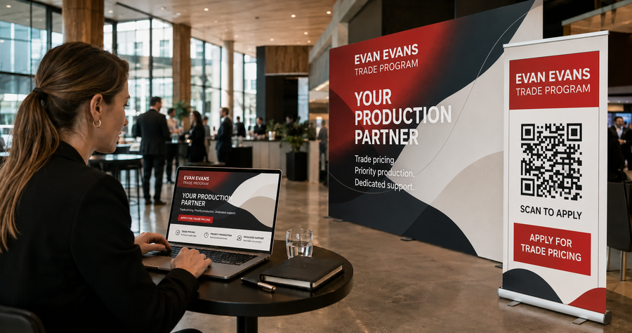 Marketing manager reviewing the Evan Evans Trade Program digital campaign beside a matching media wall and QR-enabled pull-up banner.
