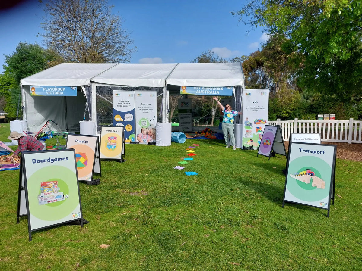 Michelle Loft's market stall setup with Evan Evans signage solutions for Toy Libraries Australia, showcasing board games, puzzles, and transport toys. | Custom signage by Evan Evans Australia
