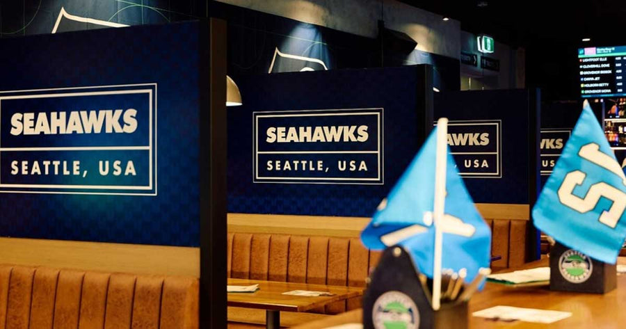 Booth seating inside Hickens Hotel featuring blue printed Seattle Seahawks divider panels and table-top event decorations.