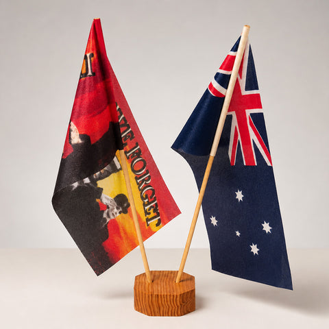 Two small tabletop flags on wooden sticks mounted in a round wooden base. The left flag is red, black, and yellow with the words 'ANZEM' and 'THE FORGET'.