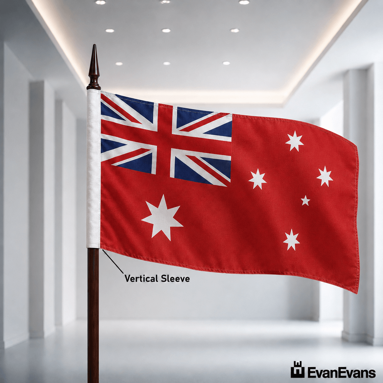 An Australian flag mounted on a flagpole, shown waving in a bright modern indoor hallway. The image includes a text label pointing to the white vertical sleeve on the pole and a watermark in the bottom right reading EvanEvans.