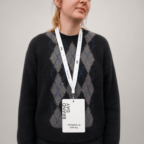 A woman wearing a dark charcoal knit sweater with a blue and gray argyle pattern, featuring a white lanyard with a branded 'BRAND DAY' physical ID card.
