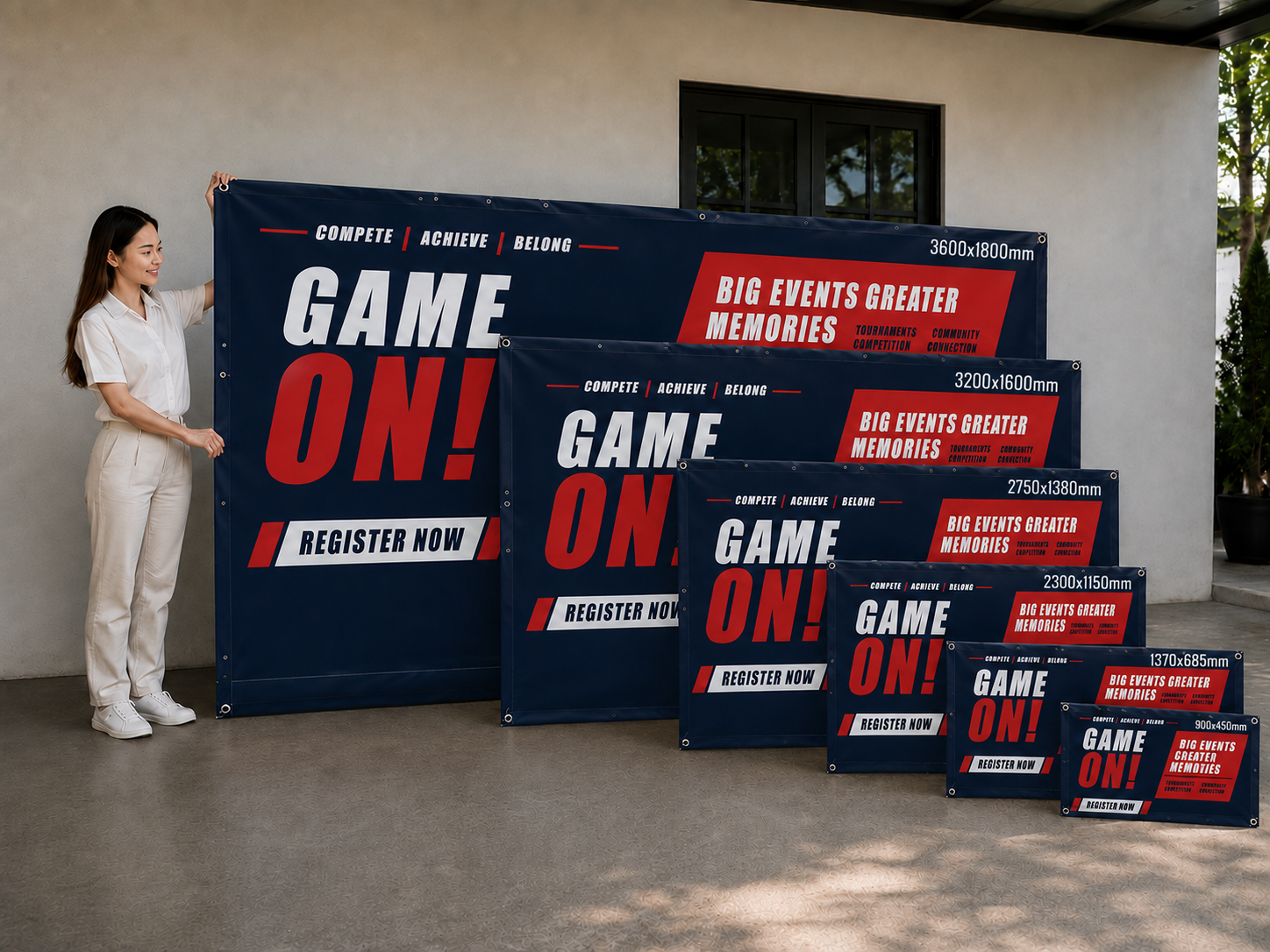 A woman in a white uniform stands beside a large navy blue event banner that reads “GAME ON!” and “REGISTER NOW,” with multiple matching smaller banners arranged in descending size on a patio in front of a building.