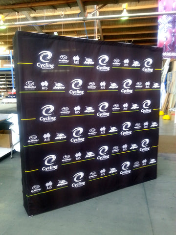 A large black fabric backdrop banner with repeated white Cycling Australia logos and small sponsor logos, photographed standing in a warehouse or studio space.