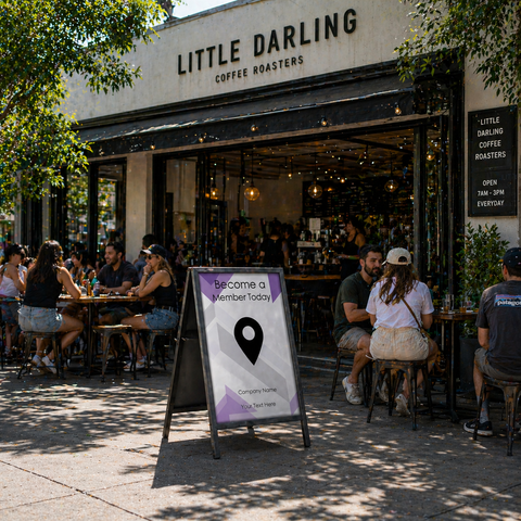 People sitting outside a coffee shop named 'Little Darling Coffee Roasters' with a sign inviting people to become members.