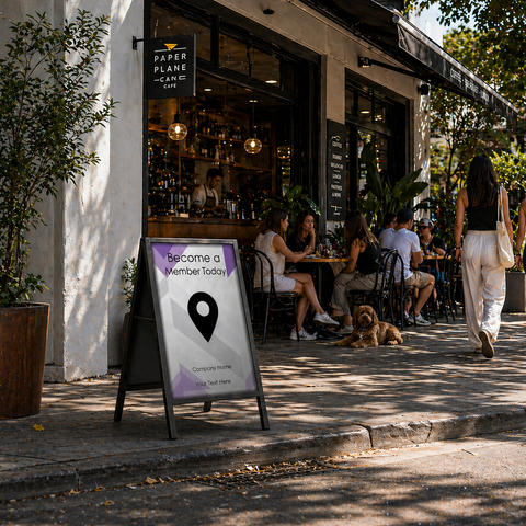 People sitting outside a cafe with a sign advertising membership on a sidewalk.