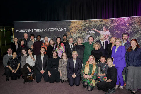 A group of people posing in front of a large 'Melbourne Theatre Company' backdrop banner at what appears to be an event or premiere.
