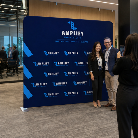 Two people posing in front of an 'Amplify' branded backdrop in a conference setting.