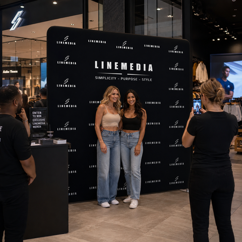 Two women posing in front of a LINEMEDIA branded backdrop with a third person taking a photo.