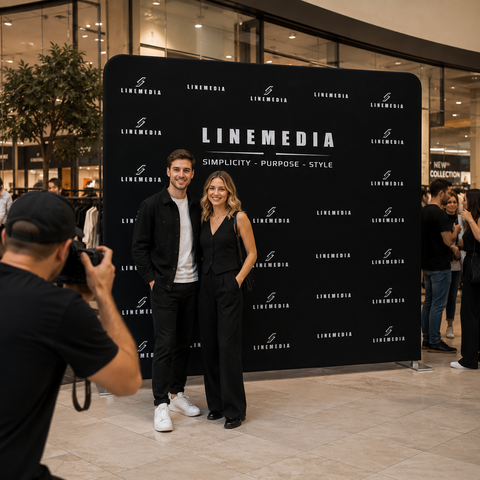 Two people posing in front of a LINEMEDIA branded backdrop with a photographer taking their picture.