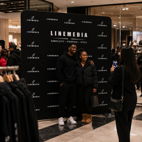 Two people posing in front of a LINEMEDIA branded backdrop in a store.