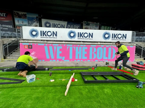 A bright pink wall installation with the message "We, The Bold" enhances the aesthetics of Ikon Park, emphasizing team spirit and bold creativity.